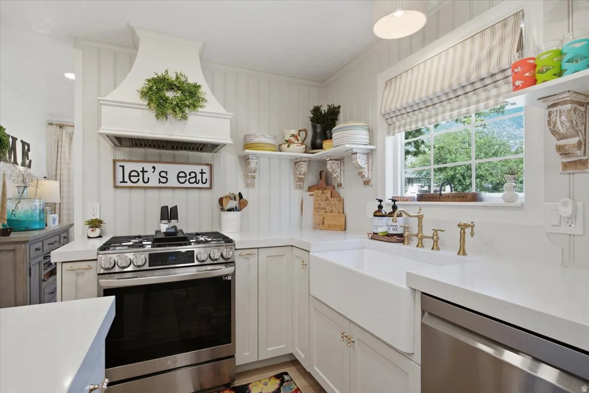 White cabinetry with brass hardware, a stainless steel range, and a white farmhouse sink
