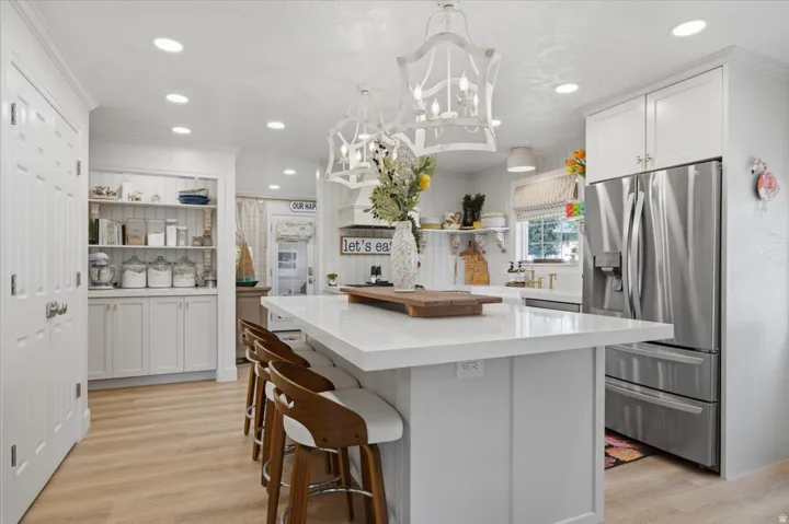 Kitchen featuring a large central island with seating, white shaker cabinetry, recessed lighting, stainless steel refrigerator, and wood-finish flooring