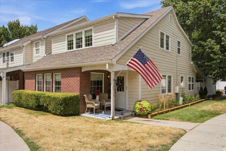 Exterior featuring tan siding, red brick accents, a gabled roofline, a covered front porch, and a sidewalk entrance