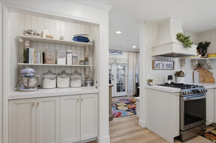 Kitchen featuring beadboard paneling, built-in shelving, white cabinetry with gold hardware, a range hood, and stainless steel stove