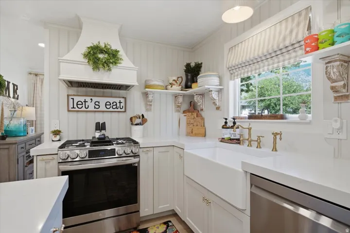 White cabinetry with brass hardware, a stainless steel range, and a white farmhouse sink