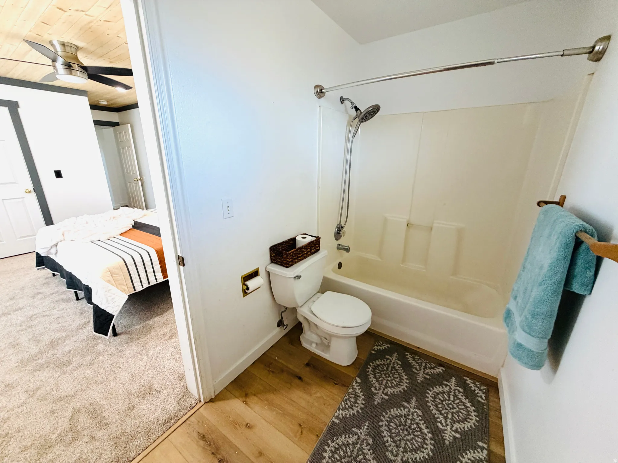 Bathroom with wood-finish flooring, a white toilet, and a combined shower-tub unit