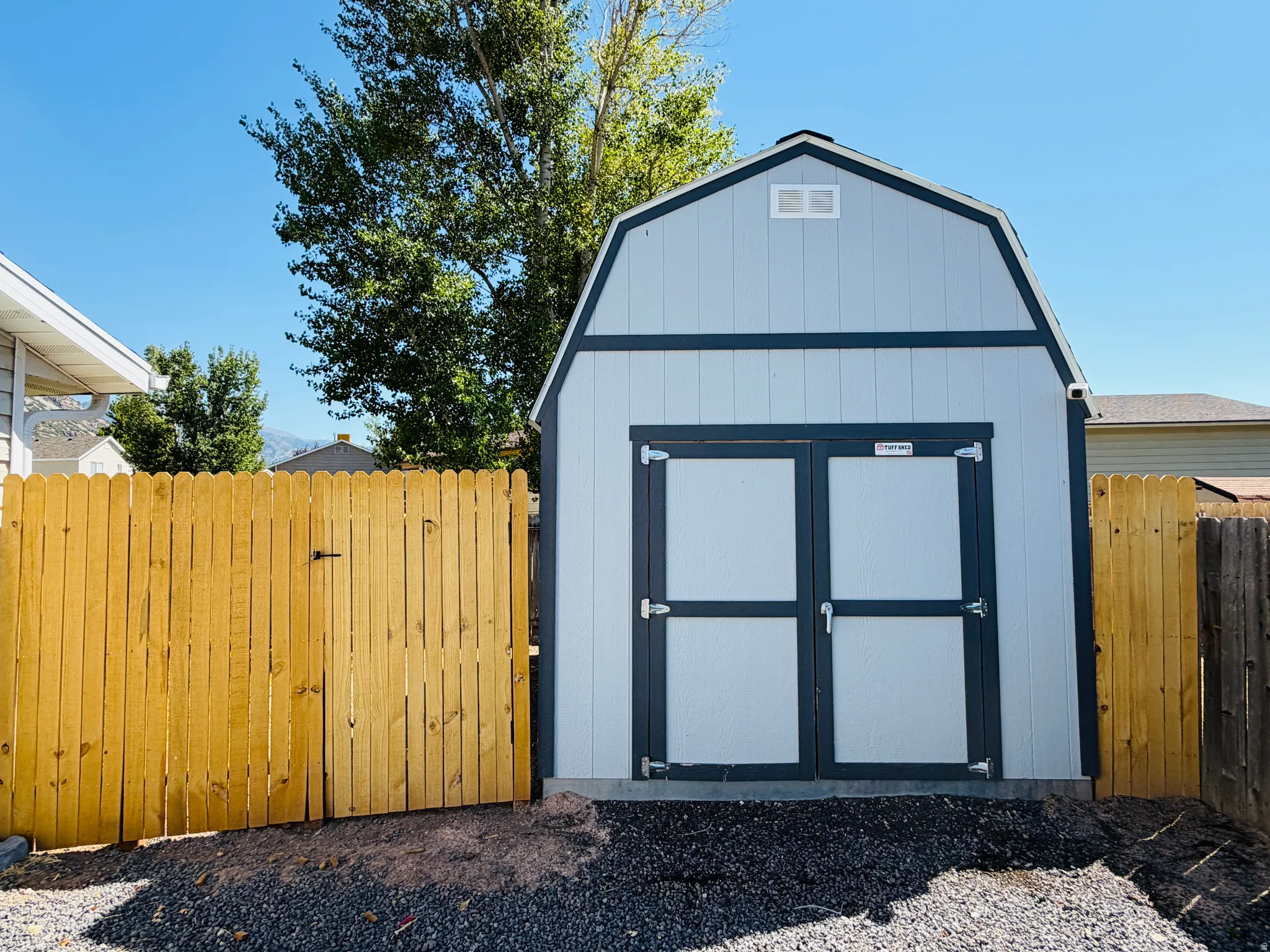 Light blue utility shed with dark trim, dual front doors, and a gable roof with a small vent
