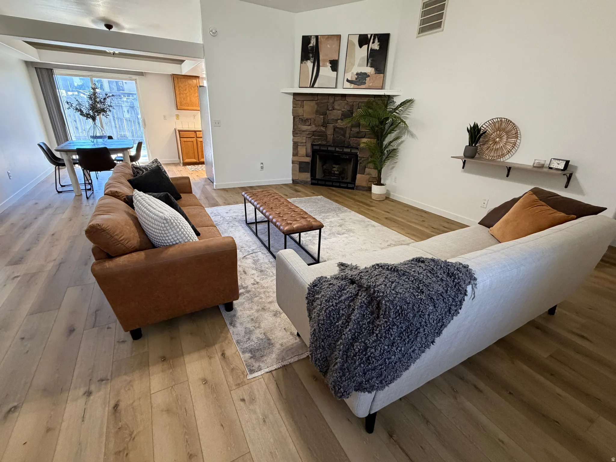 Spacious living area featuring light wood-finish flooring, a stone-surround fireplace with a black insert, and a vaulted ceiling