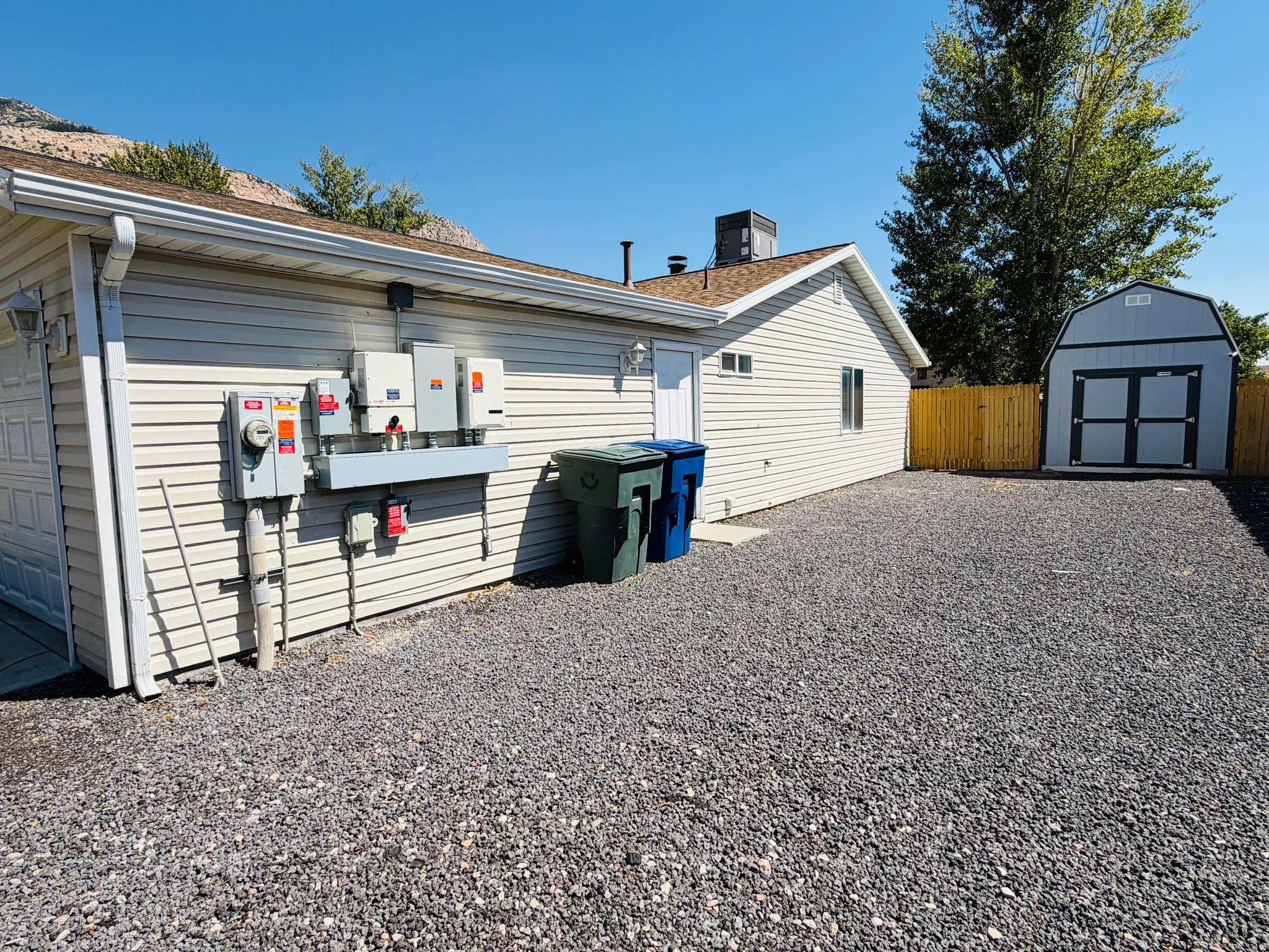 Gravel parking area featuring a detached storage shed, privacy fencing, and exterior wall siding
