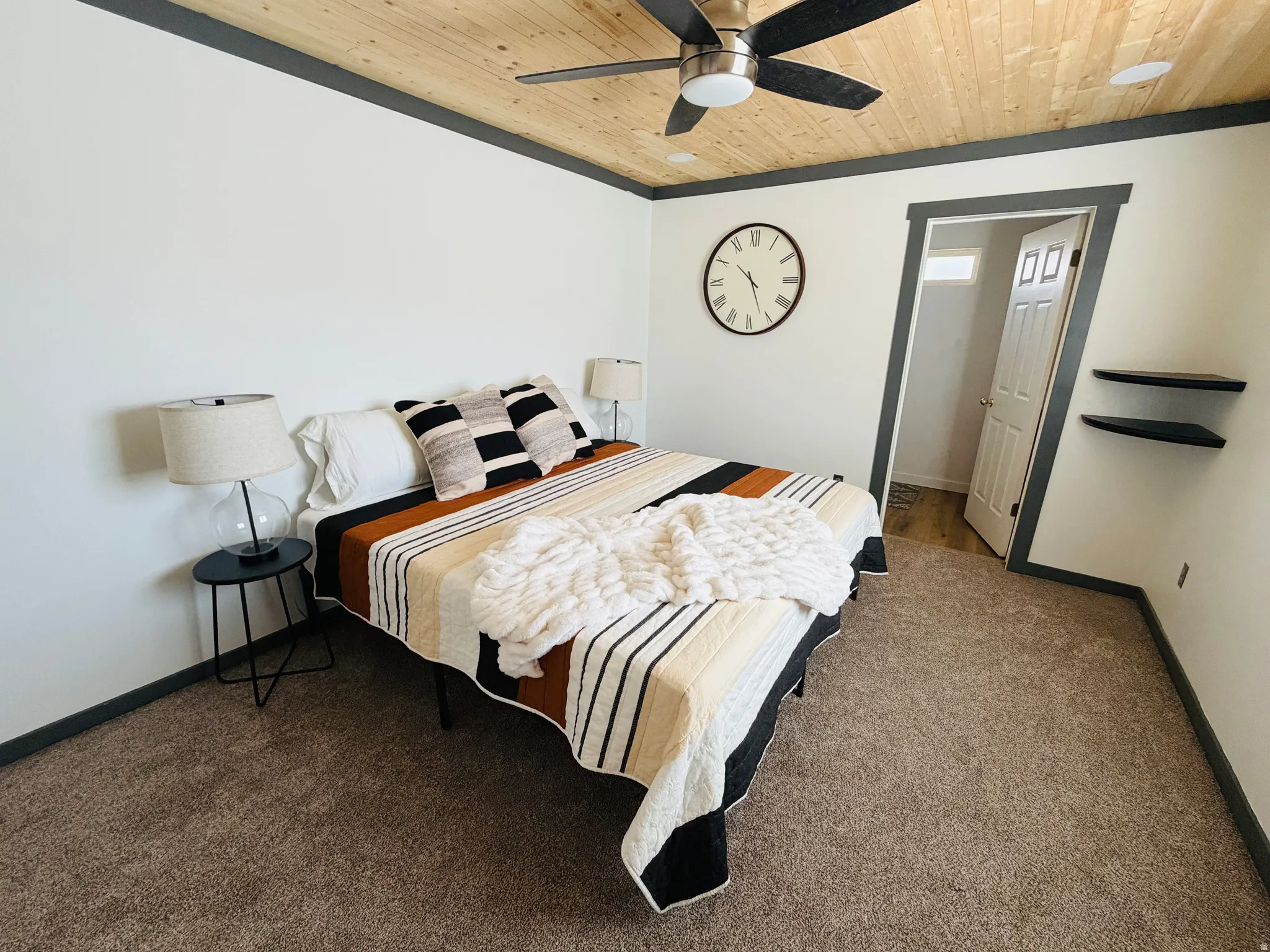 Carpeted room featuring a wood-panel ceiling, dark trim, a ceiling fan with integrated lighting, and floating wall shelves