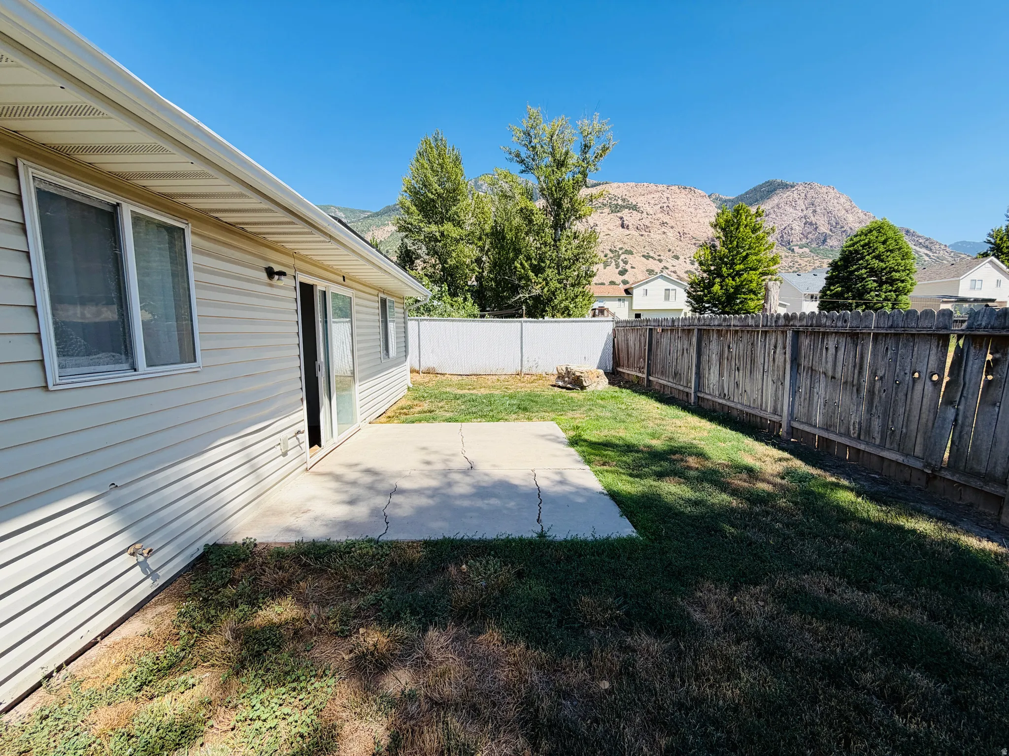 Rear exterior featuring light-colored siding, a concrete patio, and a wood privacy fence
