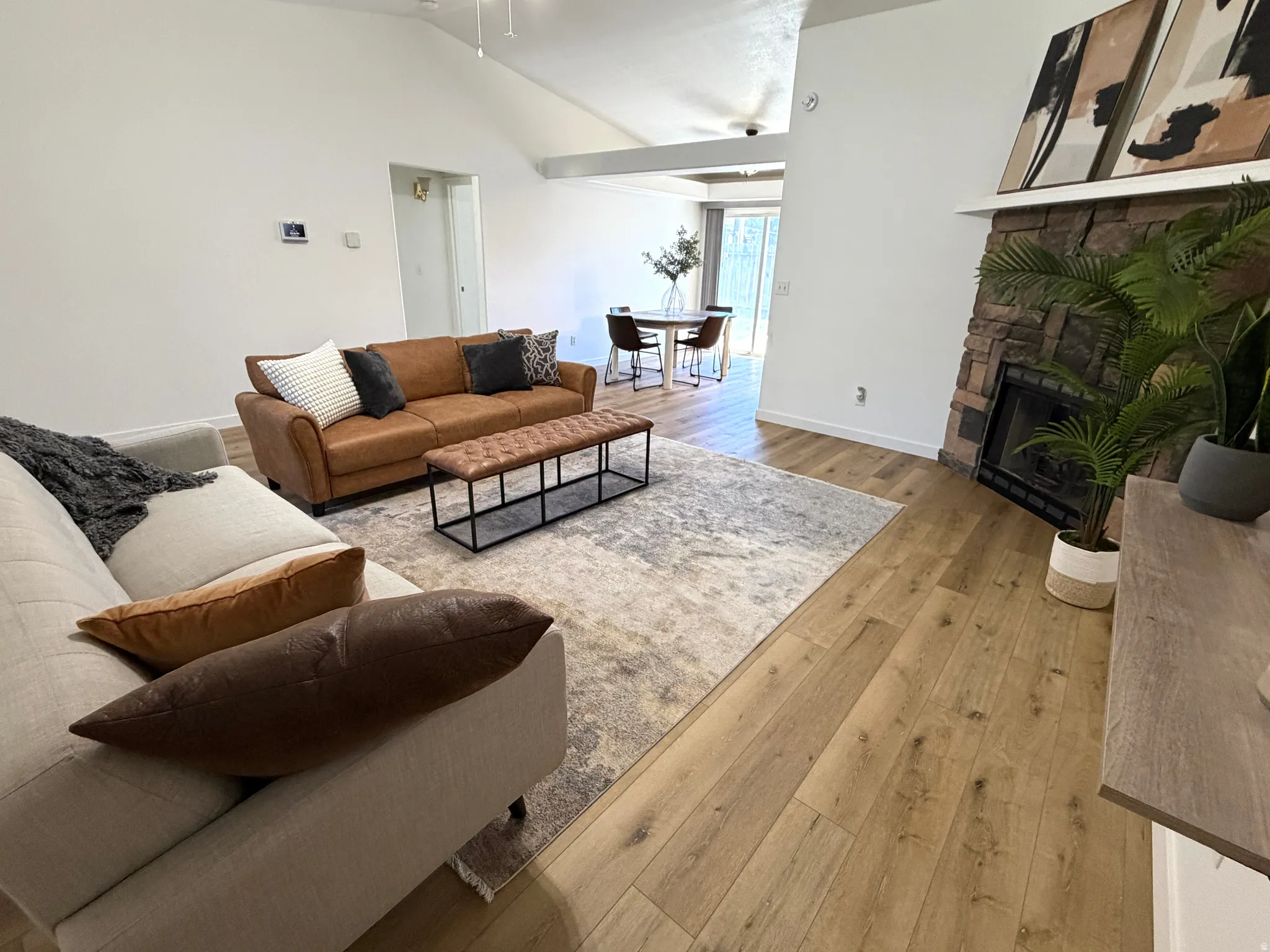 Open concept living space featuring wood-finish flooring, a vaulted ceiling, and a stone-clad fireplace