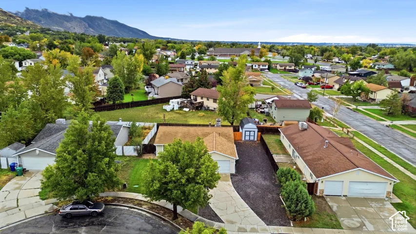 Aerial perspective featuring a shingled roof, asphalt-paved driveway, detached storage shed, grass lawn, and mountainous horizon