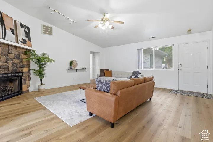 Living area featuring vaulted ceilings, wood-finish flooring, a full-height stone masonry fireplace, track lighting, and a ceiling fan