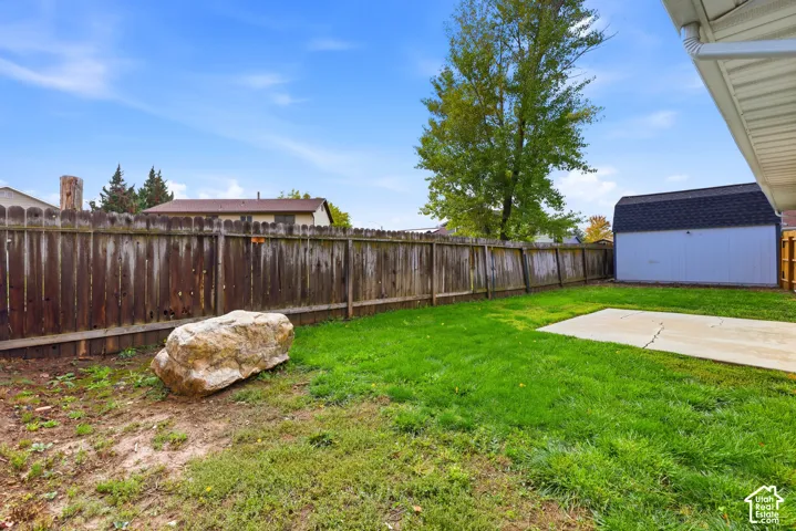 Backyard featuring a wood privacy fence, a concrete patio, a detached storage shed, and a decorative landscape boulder