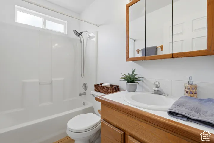 Bathroom featuring a molded composite tub and shower combination, white tile vanity countertop, wood-finish cabinetry, and a tri-fold medicine cabinet