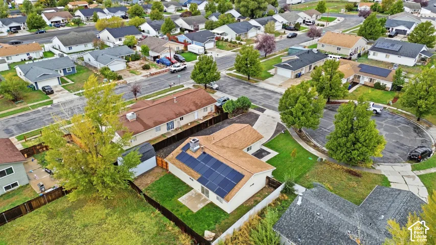 Aerial perspective featuring a residential lot with a concrete driveway, established lawn, privacy fencing, and roof-mounted solar panel array