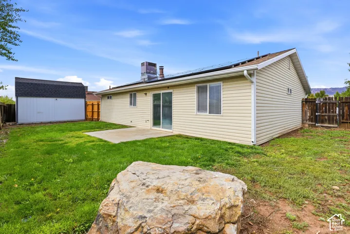 Exterior featuring light-toned horizontal siding, roof-mounted solar panels, a concrete rear patio, and a detached storage structure