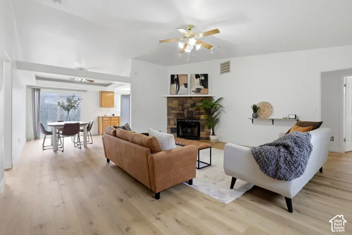 Open-concept living space featuring wood-finish flooring, a stone-faced fireplace with a mantel, and an integrated ceiling fan with lighting