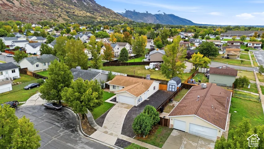 Aerial perspective featuring a detached two-car garage, concrete driveway, storage shed, and mountain backdrop