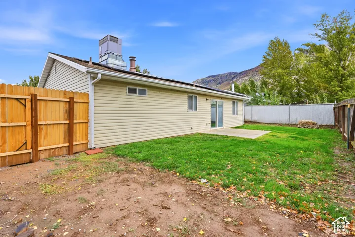 Rear exterior featuring vinyl siding, concrete patio, wood privacy fencing, and mountain backdrop