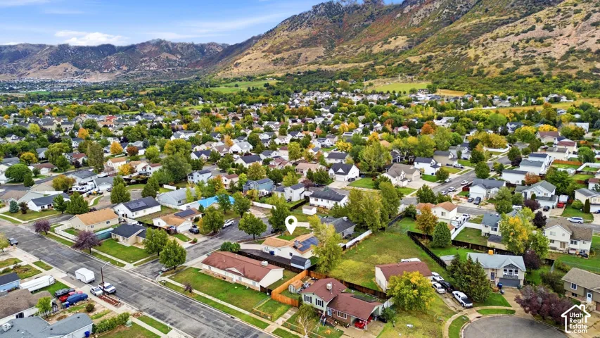 Aerial perspective featuring a residential property with roof-mounted solar panels, an attached garage, a fenced backyard, and a mountain range backdrop
