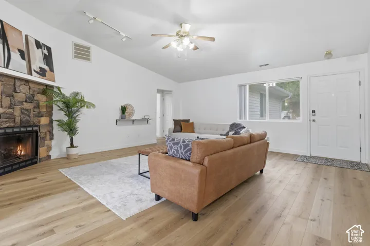 Vaulted ceiling featuring a stone-clad fireplace, wood-finish flooring, track lighting, and a ceiling fan