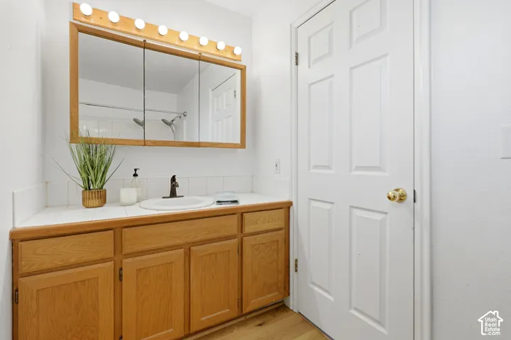 Wood-finish cabinetry, tile countertop, integrated medicine cabinet with linear light fixture, and six-panel door