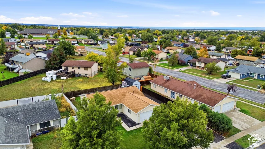 Aerial perspective of a residential property featuring a composition shingle roof, attached garage, private backyard with wood fencing, and mature trees