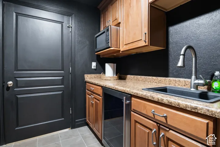Wet bar area featuring a composite sink with a gooseneck faucet, light wood cabinetry, a built-in microwave, and a beverage refrigerator