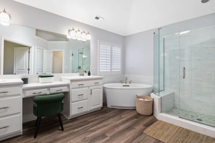 Spacious bathroom featuring wood-finish flooring, a freestanding soaking tub, and a frameless glass shower with a built-in bench