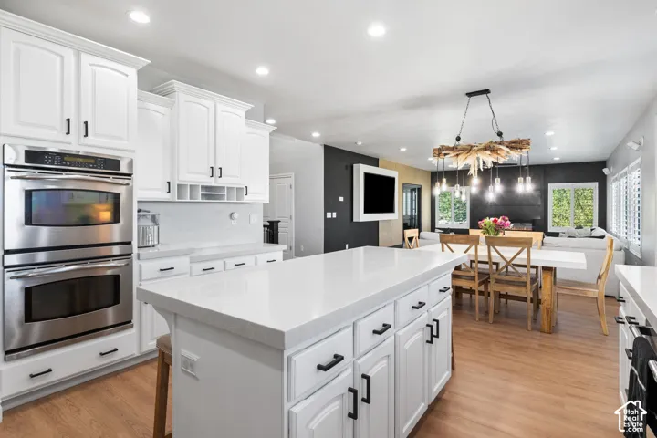 Modern kitchen featuring white cabinetry with black hardware, double stainless steel wall ovens, a large kitchen island with counter seating, and wood-finish flooring