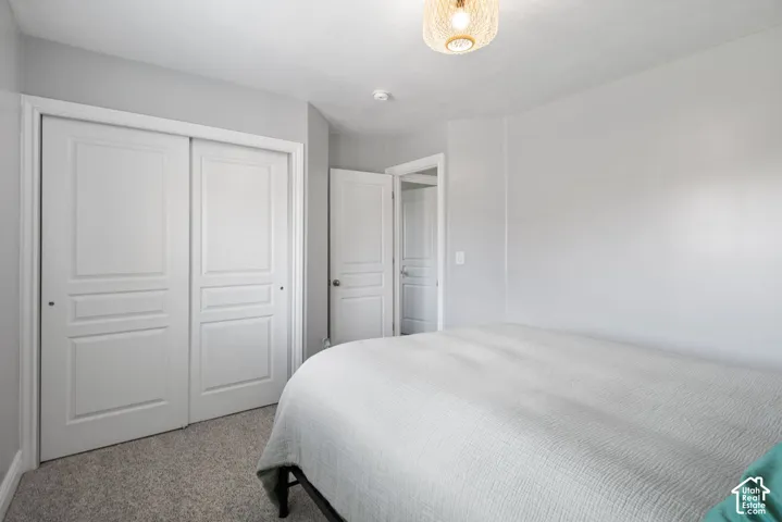 Bedroom with light gray walls, textured gray carpet, and a decorative light fixture