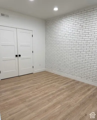 Room featuring a decorative white brick accent wall, light wood-finish flooring, and white trim