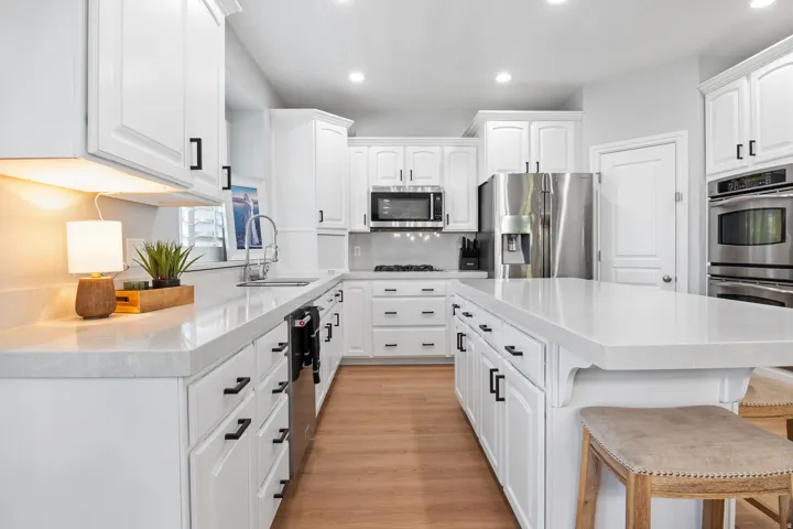Bright kitchen featuring white cabinetry, light-toned countertops, stainless steel appliances, a center island, and wood-finish flooring