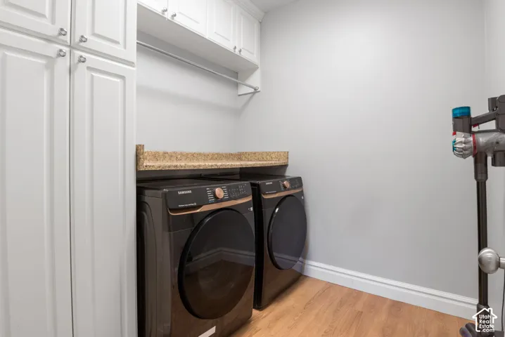 Dedicated laundry area featuring a front-loading washer and dryer, under-cabinet storage, a granite-finish countertop, and wood-finish flooring