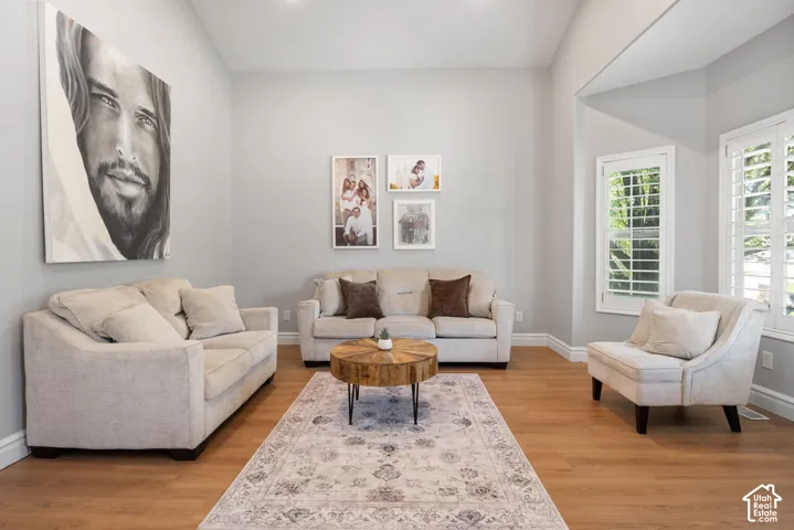 Living area featuring vaulted ceilings, light wood-finish flooring, white plantation shutters, and light grey wall tones