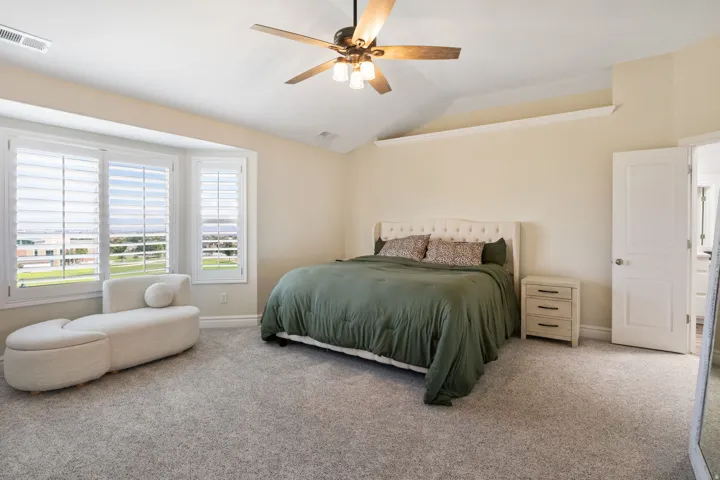 Bedroom featuring a bay window with plantation shutters, soft gray carpeting, a multi-speed ceiling fan, and access to an adjoining bathroom