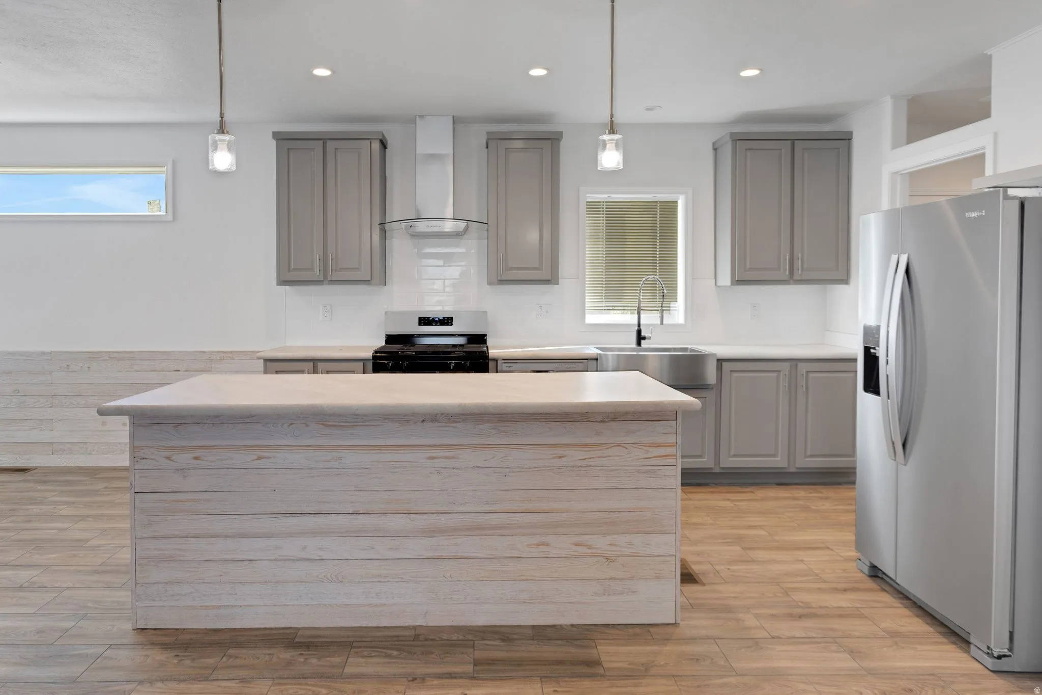 Spacious kitchen featuring a large shiplap island with a light-toned countertop, gray cabinetry, stainless steel appliances, and wood-finish flooring