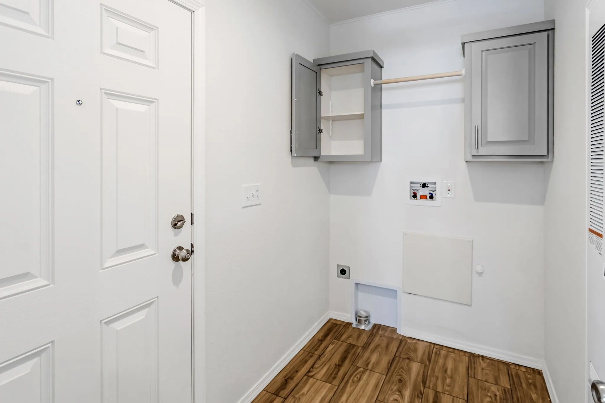 Dedicated utility area featuring wood-finish flooring, white walls, and built-in gray cabinetry for storage