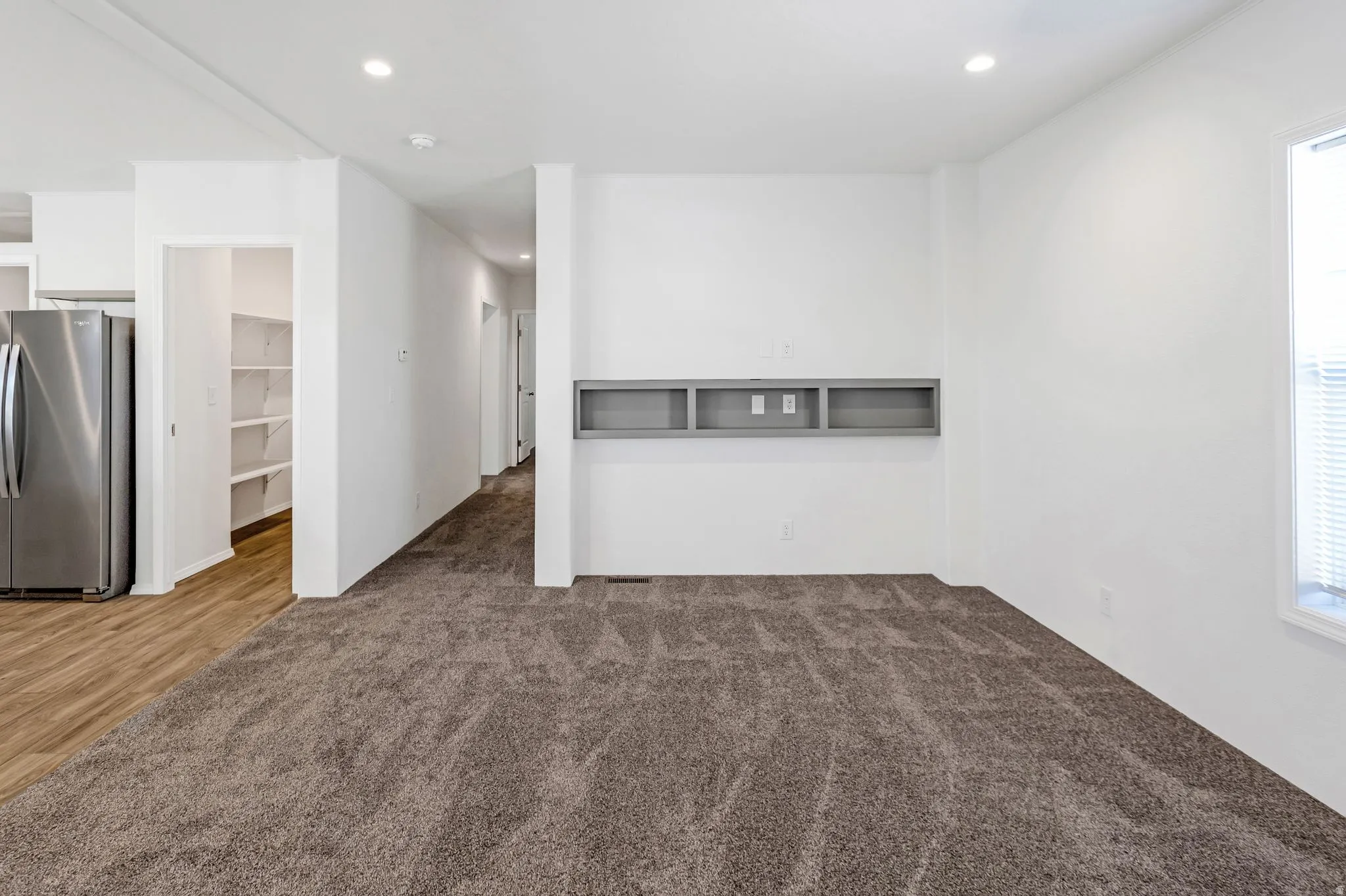 Carpeted living area with recessed lighting, a built-in media console, and a window with blinds