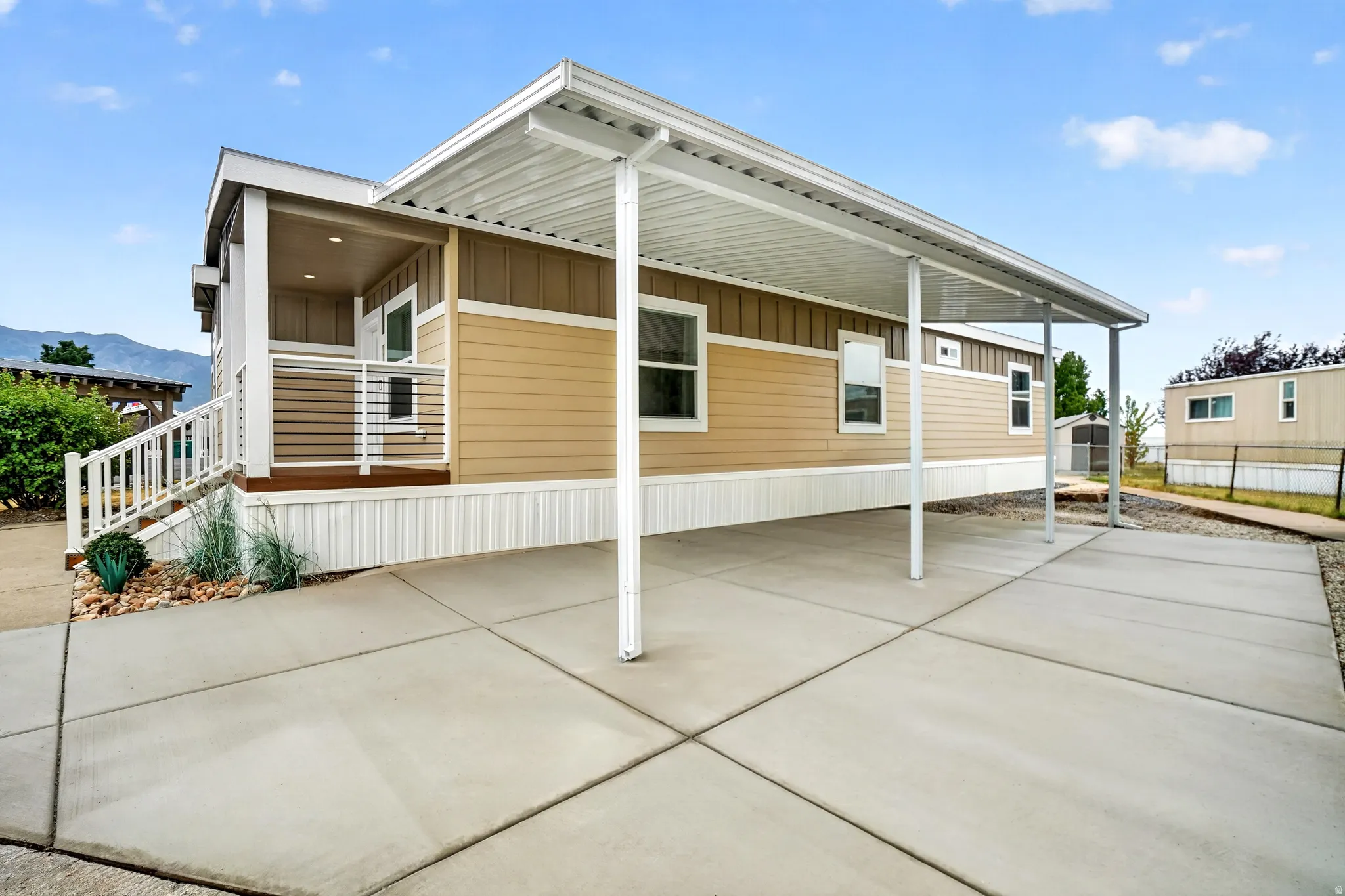 Exterior featuring a covered front porch, tan siding, white trim, a concrete driveway with a carport, and minimal landscaping