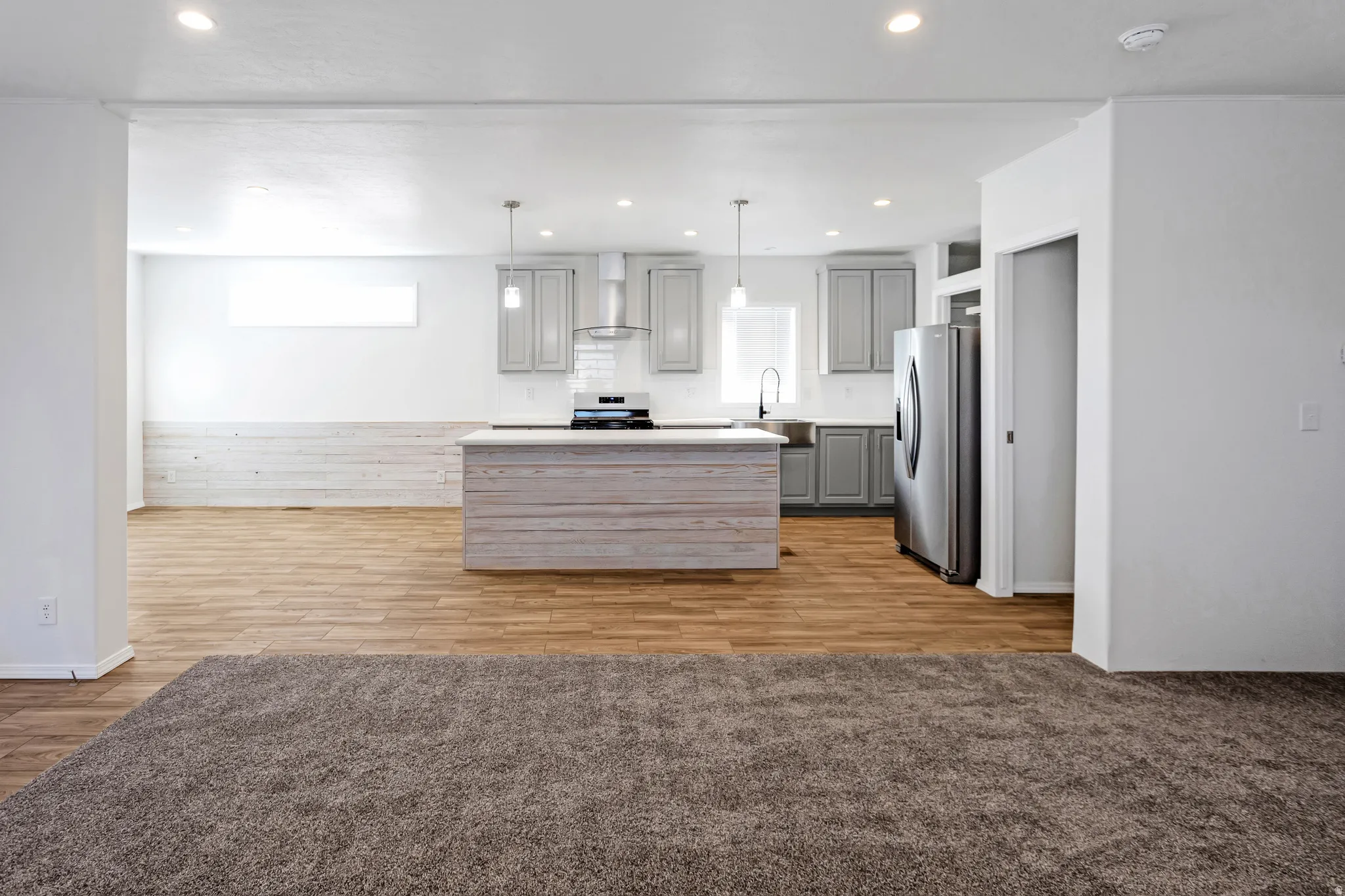 Open-concept kitchen and living area featuring wood-finish flooring, a kitchen island with stone countertop, stainless steel appliances, pendant lighting, and recessed lighting