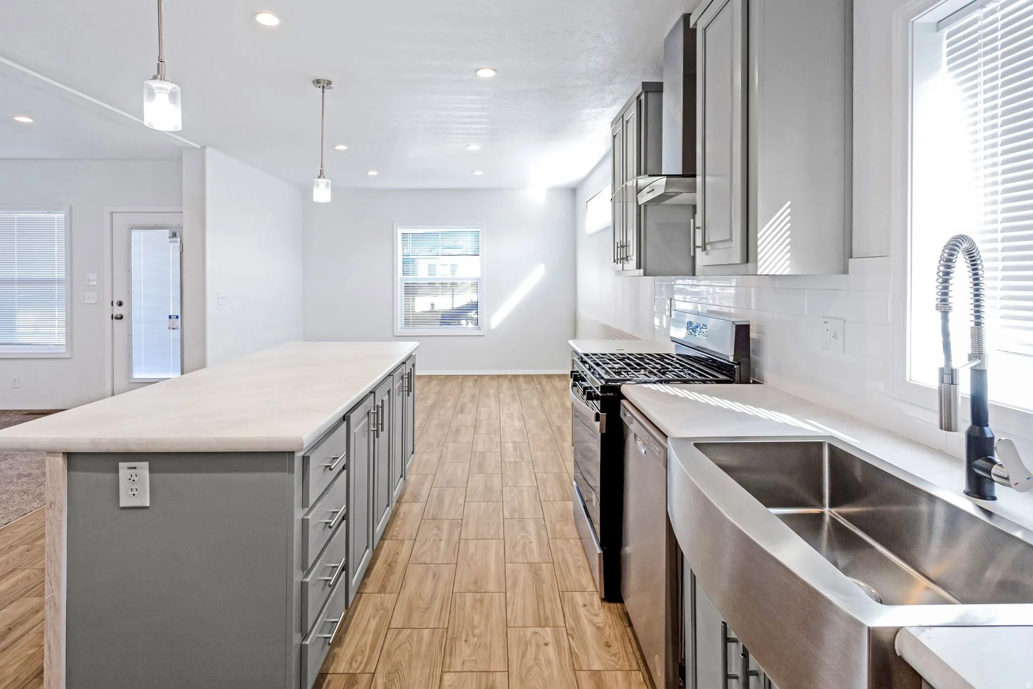 Kitchen featuring an elongated center island with storage, stainless steel apron-front sink, gas range, and wood-finish flooring