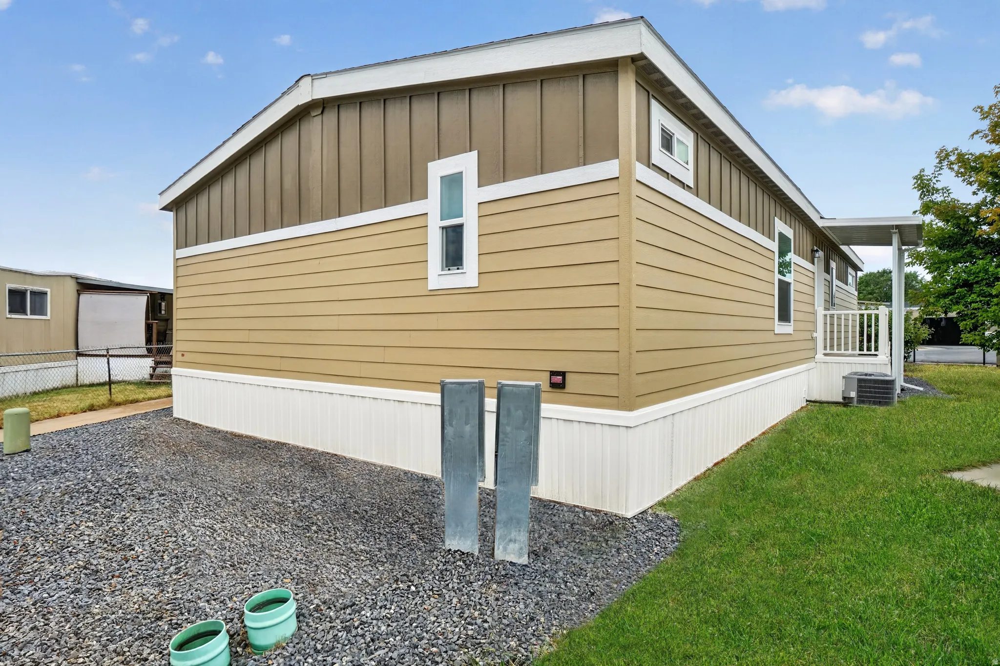 Exterior featuring tan siding with vertical brown paneling, white trim, a gravel area, and a grass lawn