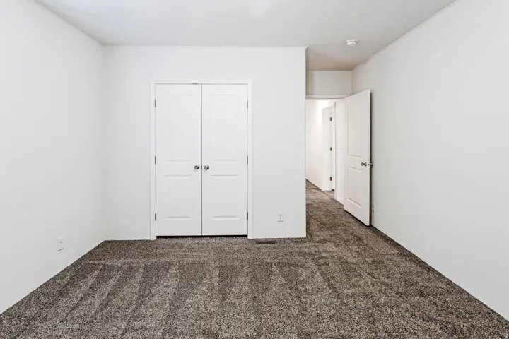 Interior room featuring neutral wall paint, grey patterned carpet, and white bi-fold doors