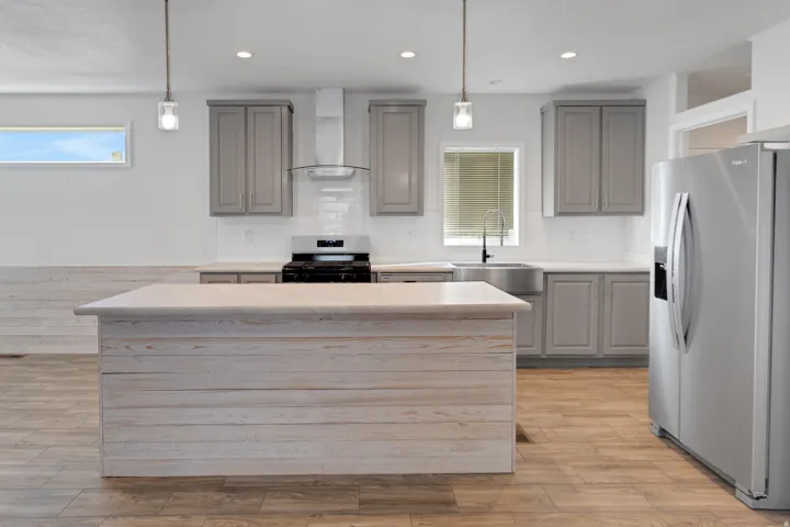 Spacious kitchen featuring a large shiplap island with a light-toned countertop, gray cabinetry, stainless steel appliances, and wood-finish flooring