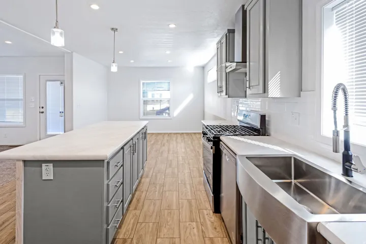 Kitchen featuring an elongated center island with storage, stainless steel apron-front sink, gas range, and wood-finish flooring