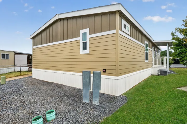 Exterior featuring tan siding with vertical brown paneling, white trim, a gravel area, and a grass lawn