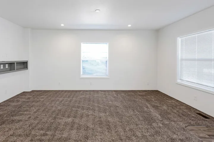 Spacious room with plush brown carpeting, recessed lighting, and two windows featuring horizontal blinds