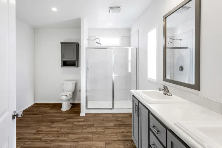 Bathroom featuring a double vanity with white countertops, wood-finish flooring, a glass-enclosed shower, and a wall-mounted medicine cabinet