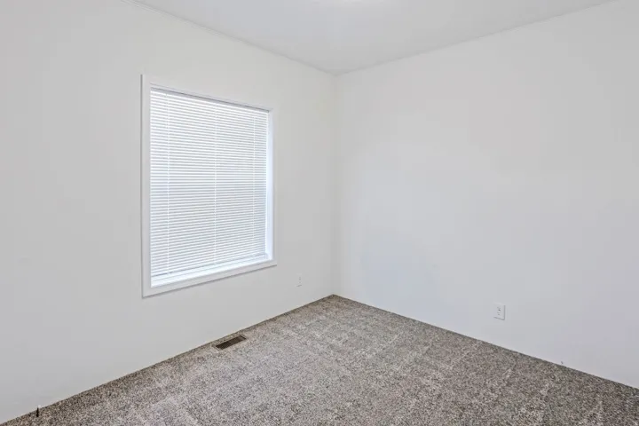 Bright interior room featuring a window with blinds, neutral wall paint, and textured carpeting