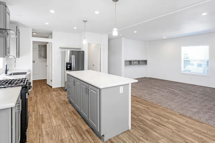 Open concept kitchen featuring an island with pendant lighting, stainless steel refrigerator, and wood-finish flooring