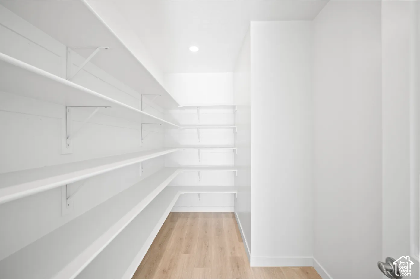 Walk-in pantry featuring extensive white shelving, recessed lighting, and wood-finish flooring
